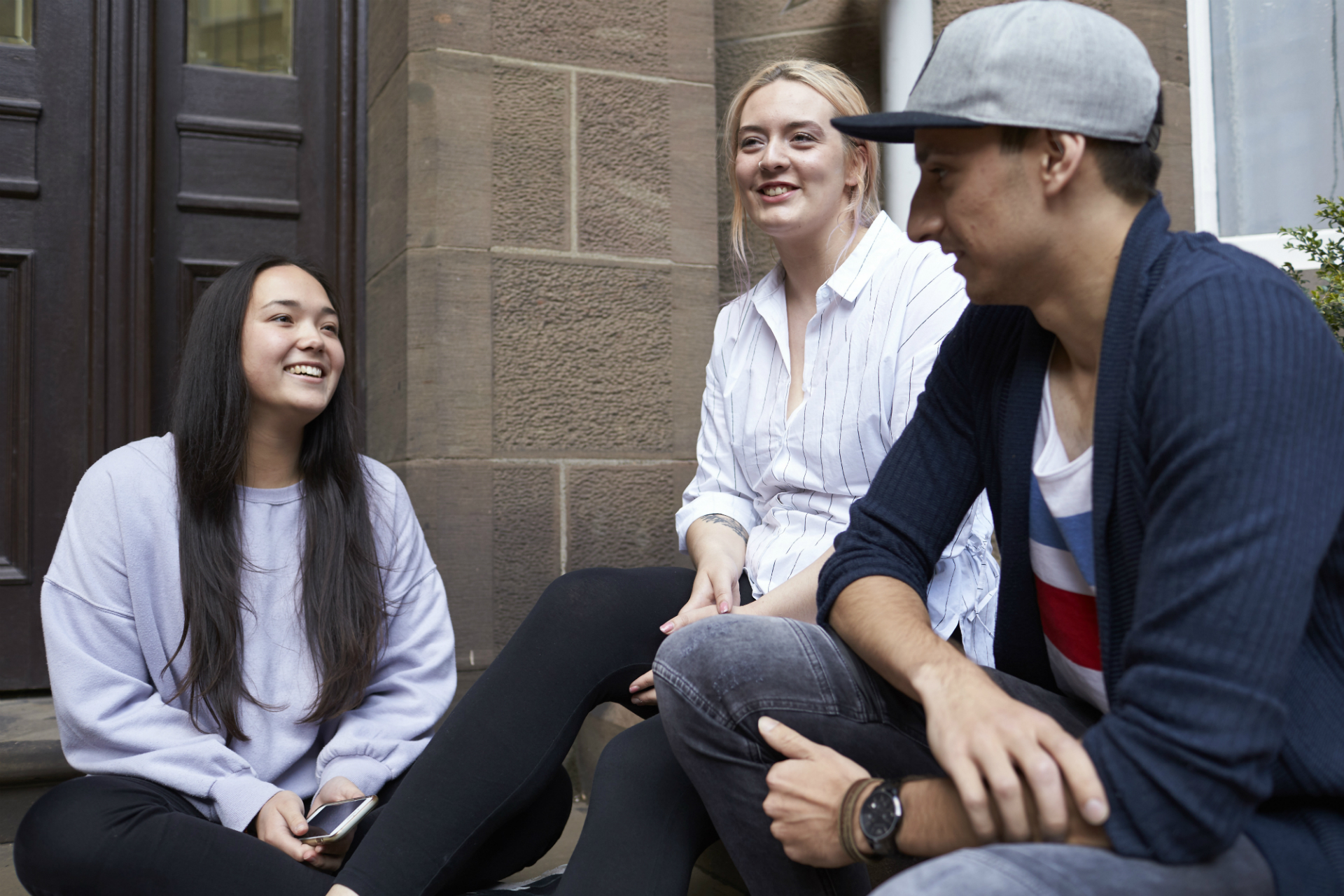 Students relaxing and chatting together outside a university building, showcasing the welcoming social spaces that support campus community life.
