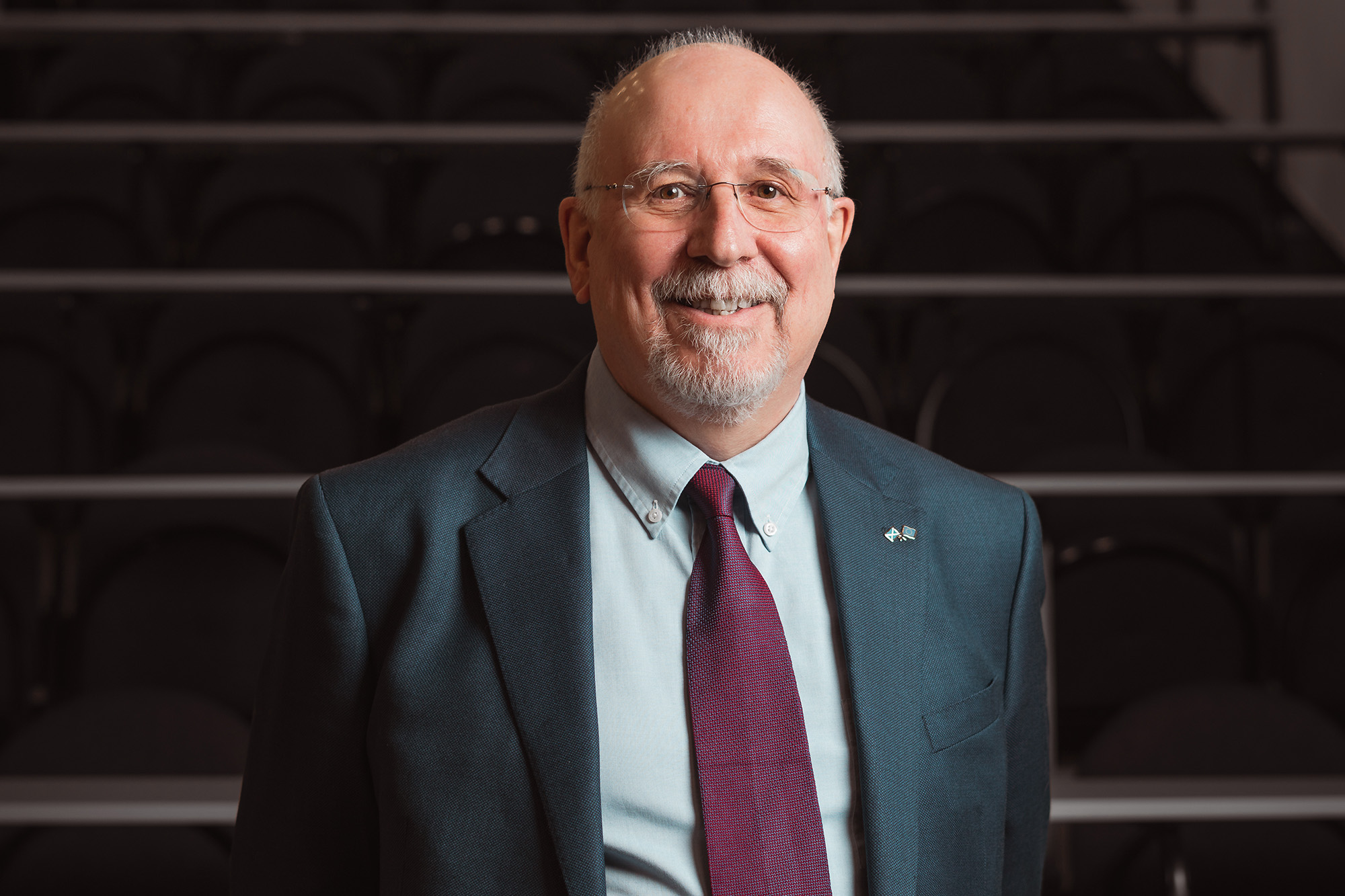 Portrait of David Brew in a navy suit and striped tie, smiling against a plain background.