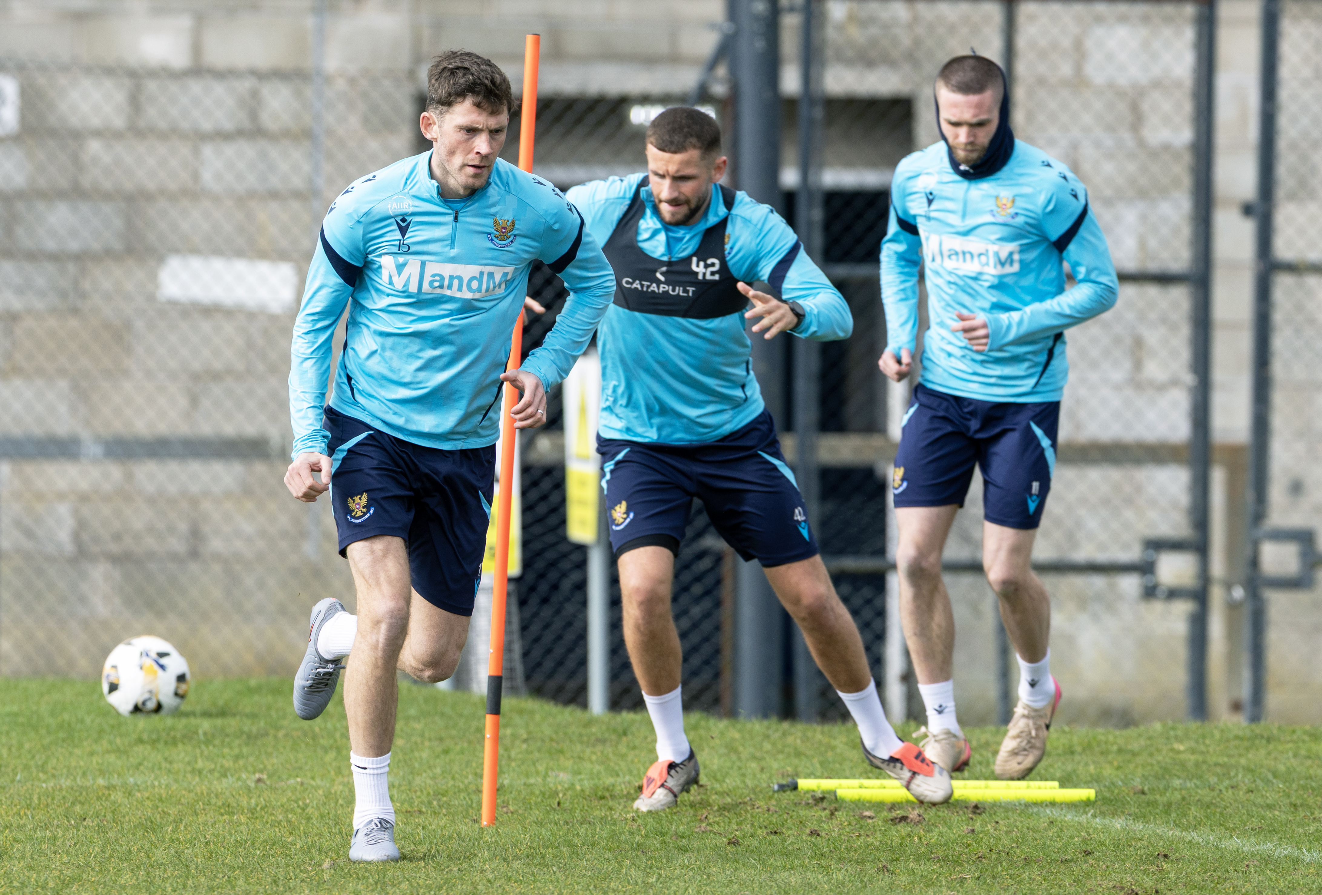 A St Johnstone football player, dressed in a sky blue top and dark blue shorts, runs around a pole during a training ground exercise. 