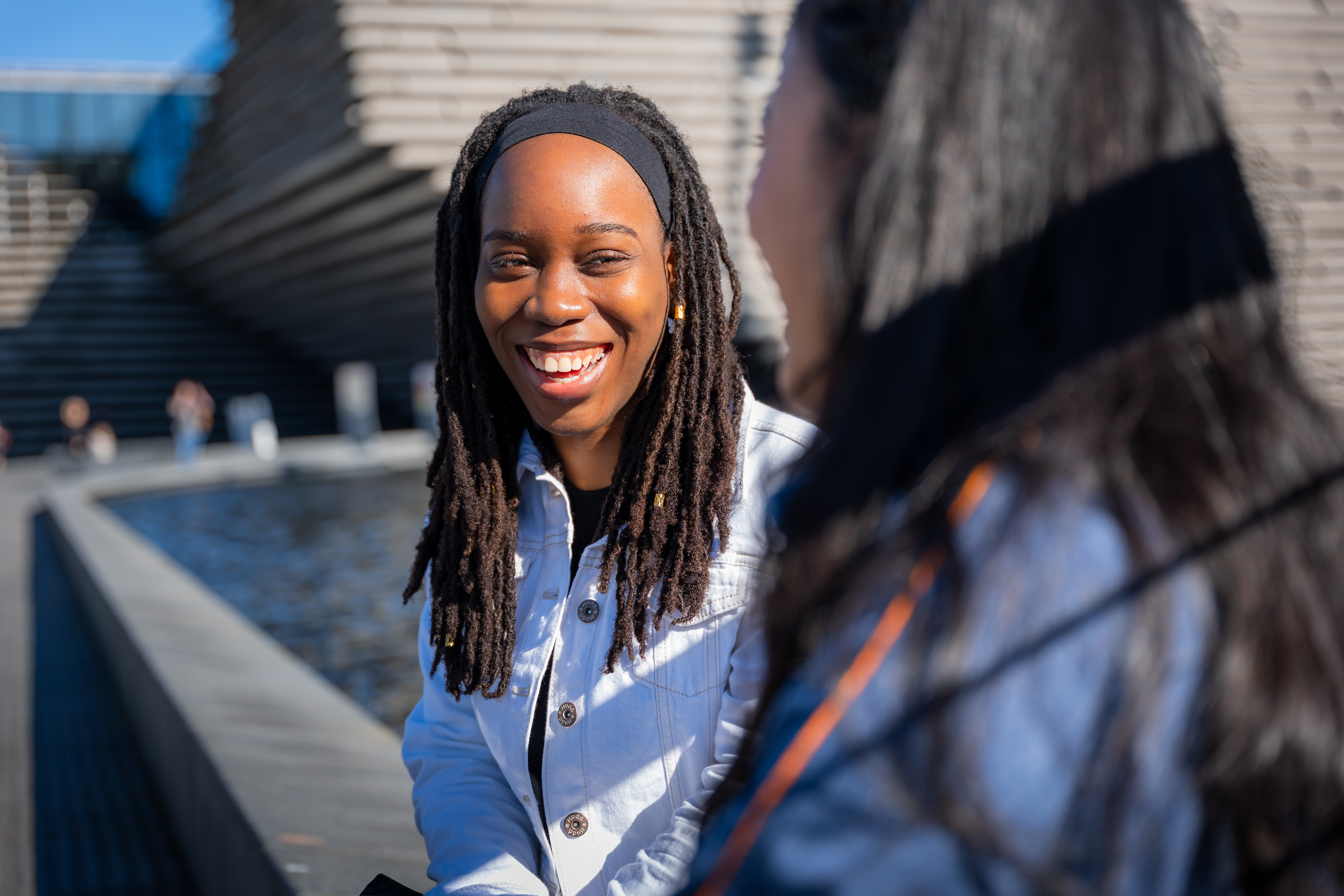 A woman sitting outside laughing and chatting to another woman sitting in front of her. 