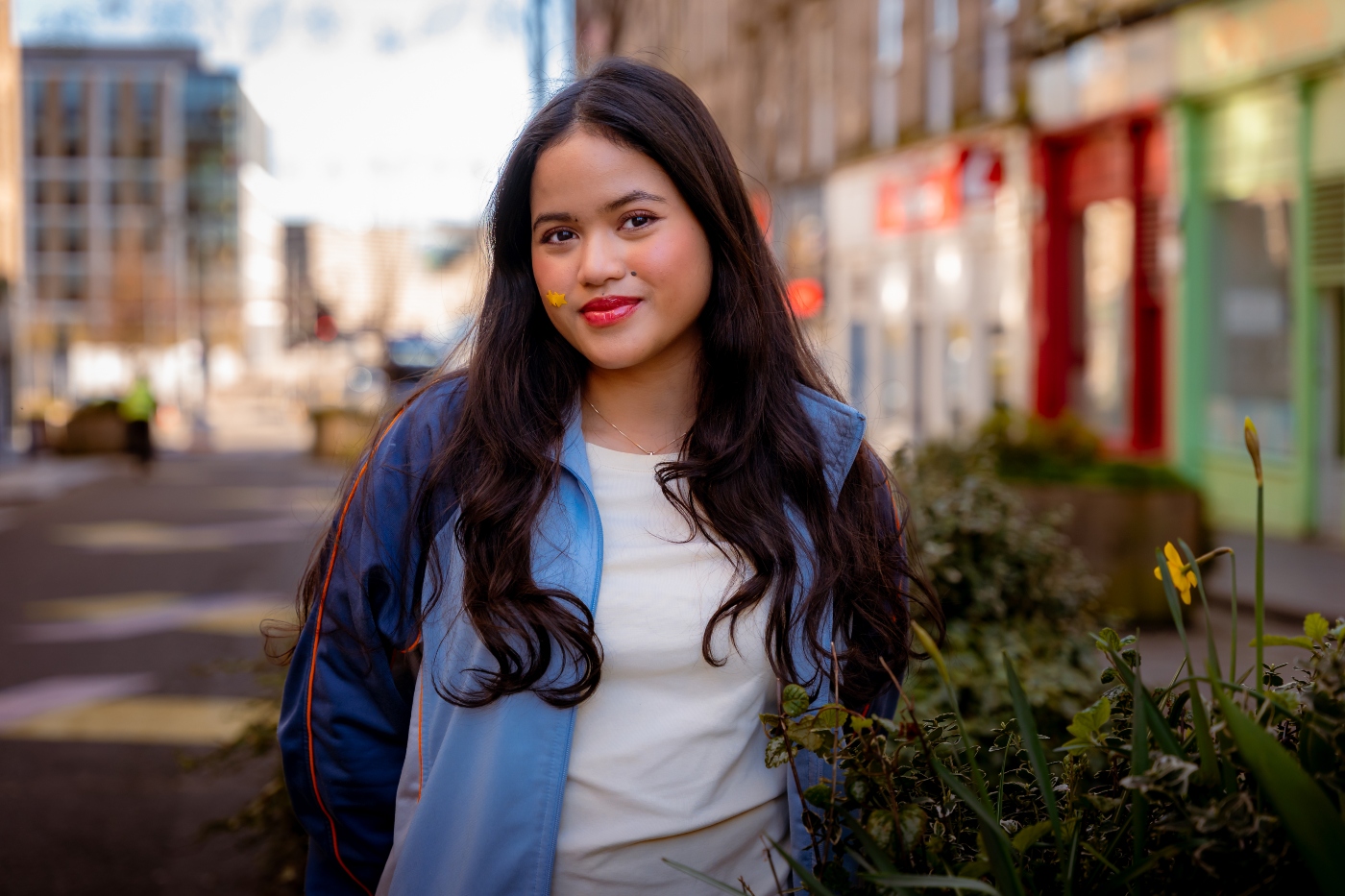 Smiling international student standing outdoors on Dundee city street with colourful buildings, representing welcoming atmosphere for prospective applicants